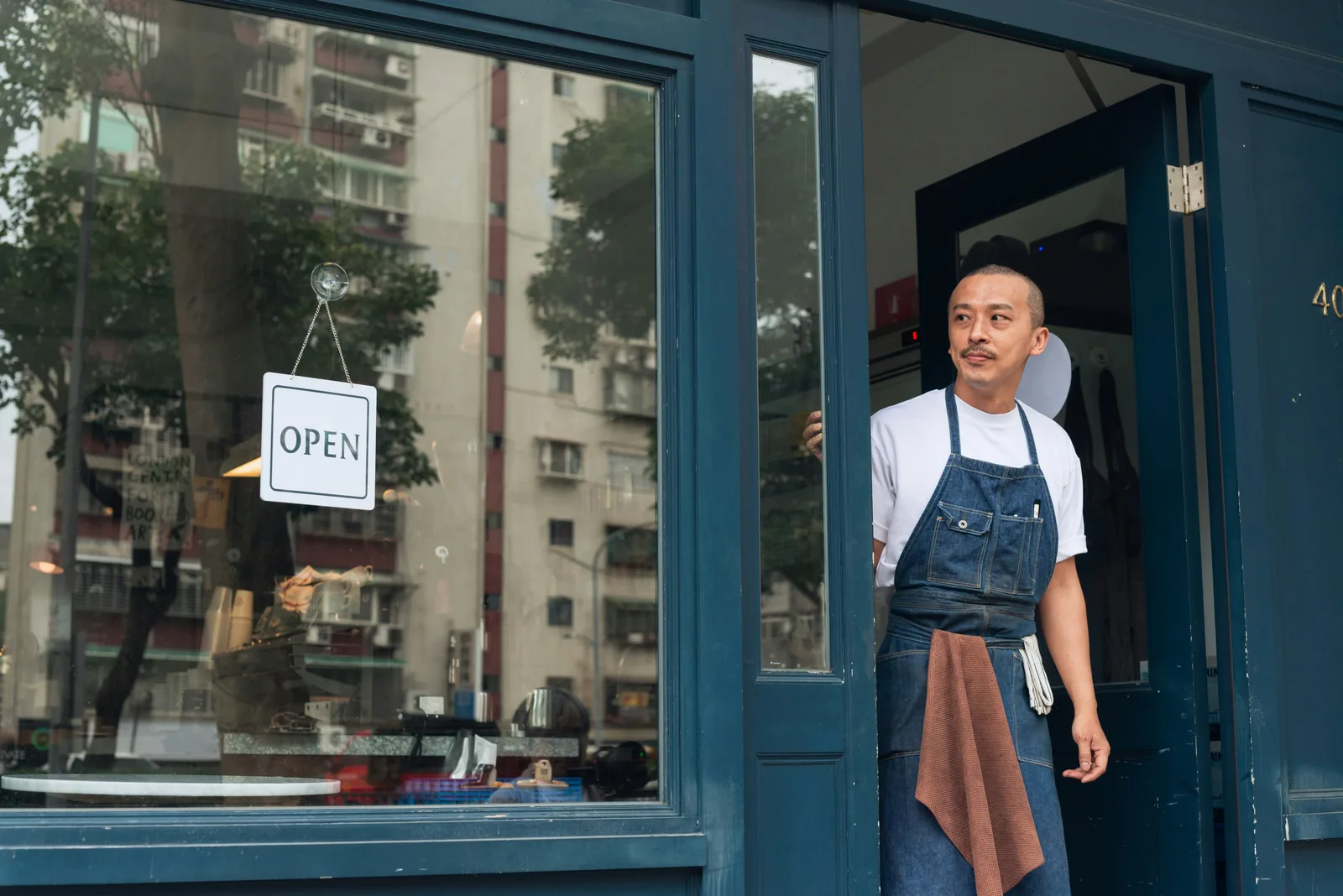 เจ้าของร้านกาแฟยืนข้างป้ายเปิดร้าน