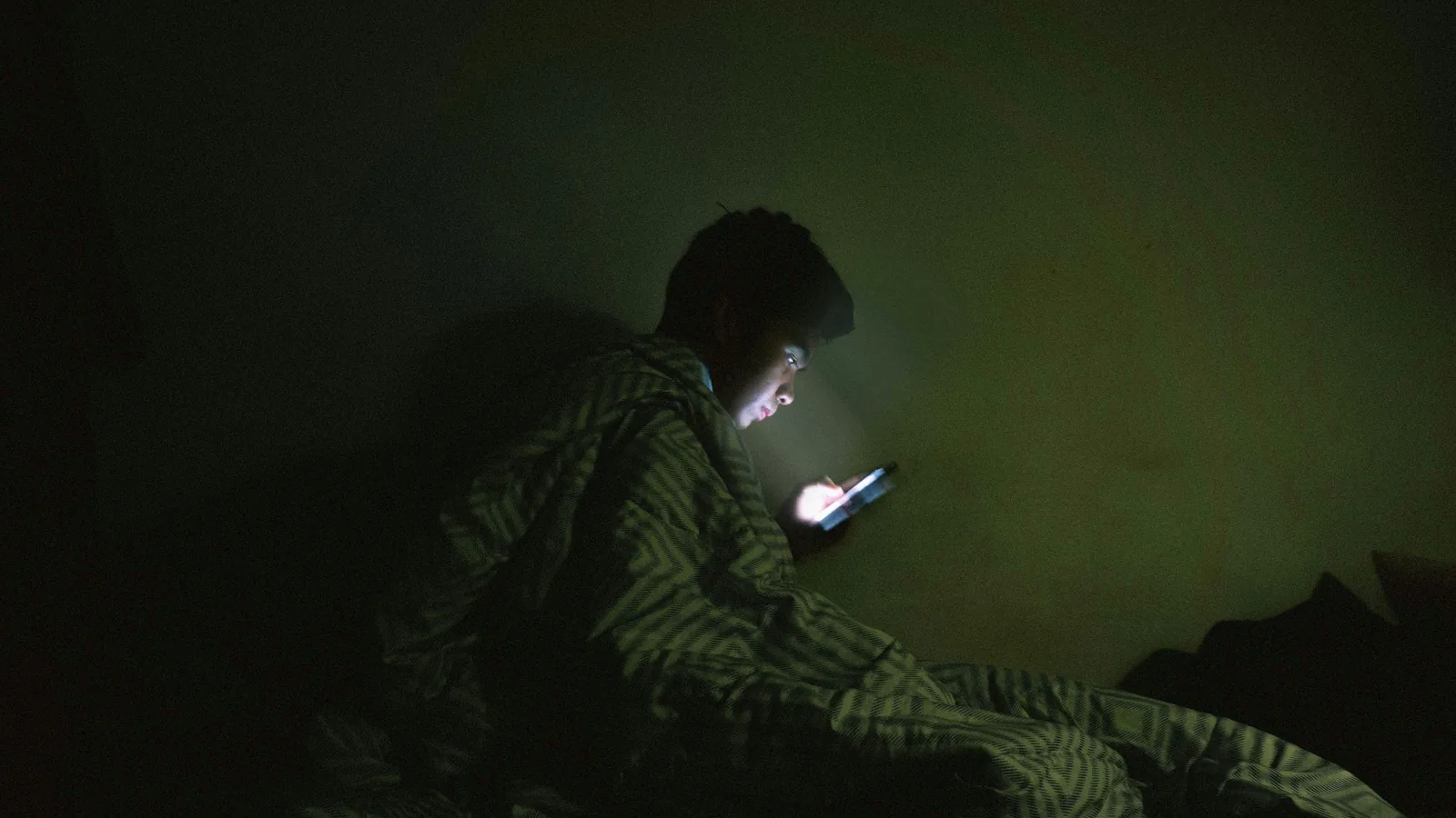 ชายหนุ่มนั่งพิมพ์ข้อความบนมือถือในห้องตอนกลางคืน