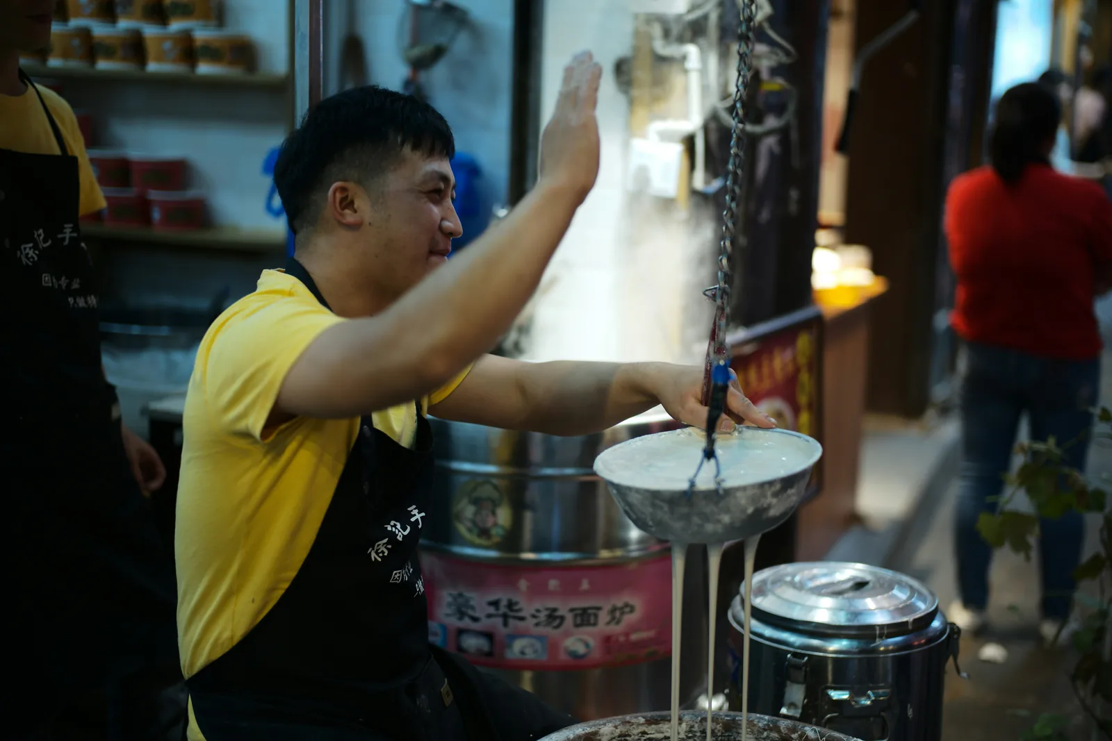 แม่ค้าร้านก๋วยเตี๋ยวยืนคนหม้อน้ำซุปที่มีไอร้อนลอยขึ้นตอนเช้ามืด