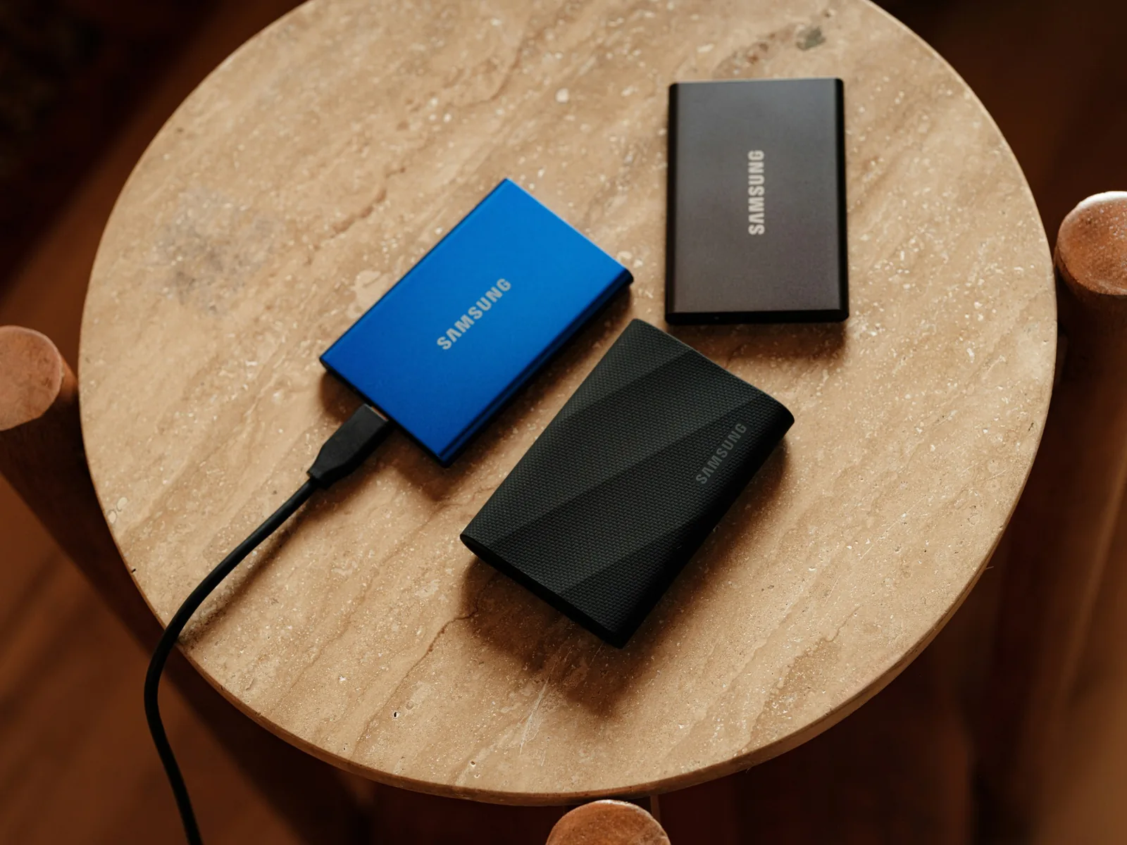SSD พกพาสามลูกสำหรับ สำรองไฟล์ วางบนโต๊ะหินกลม หนึ่งลูกเสียบสายอยู่