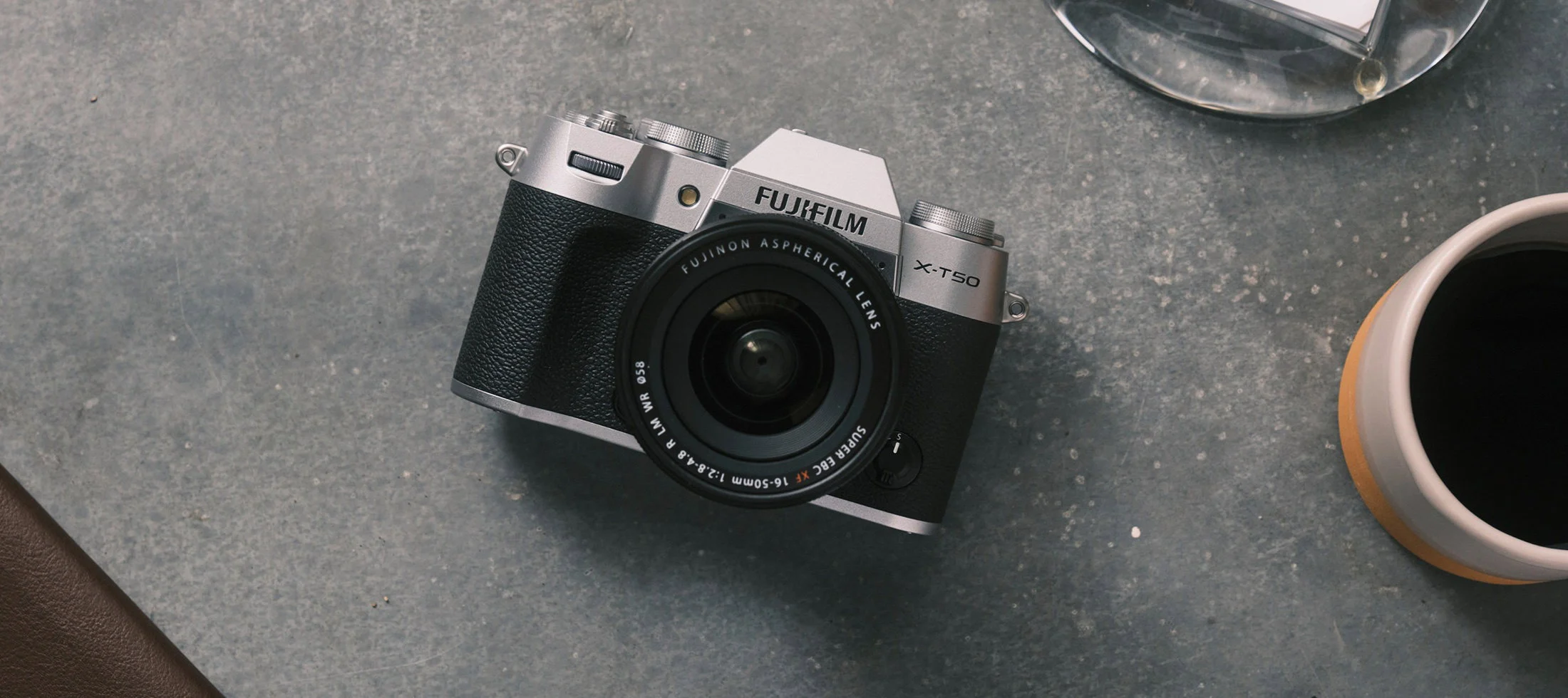 กล้อง X-T50 สีเงินวางบนโต๊ะข้างแก้วกาแฟ