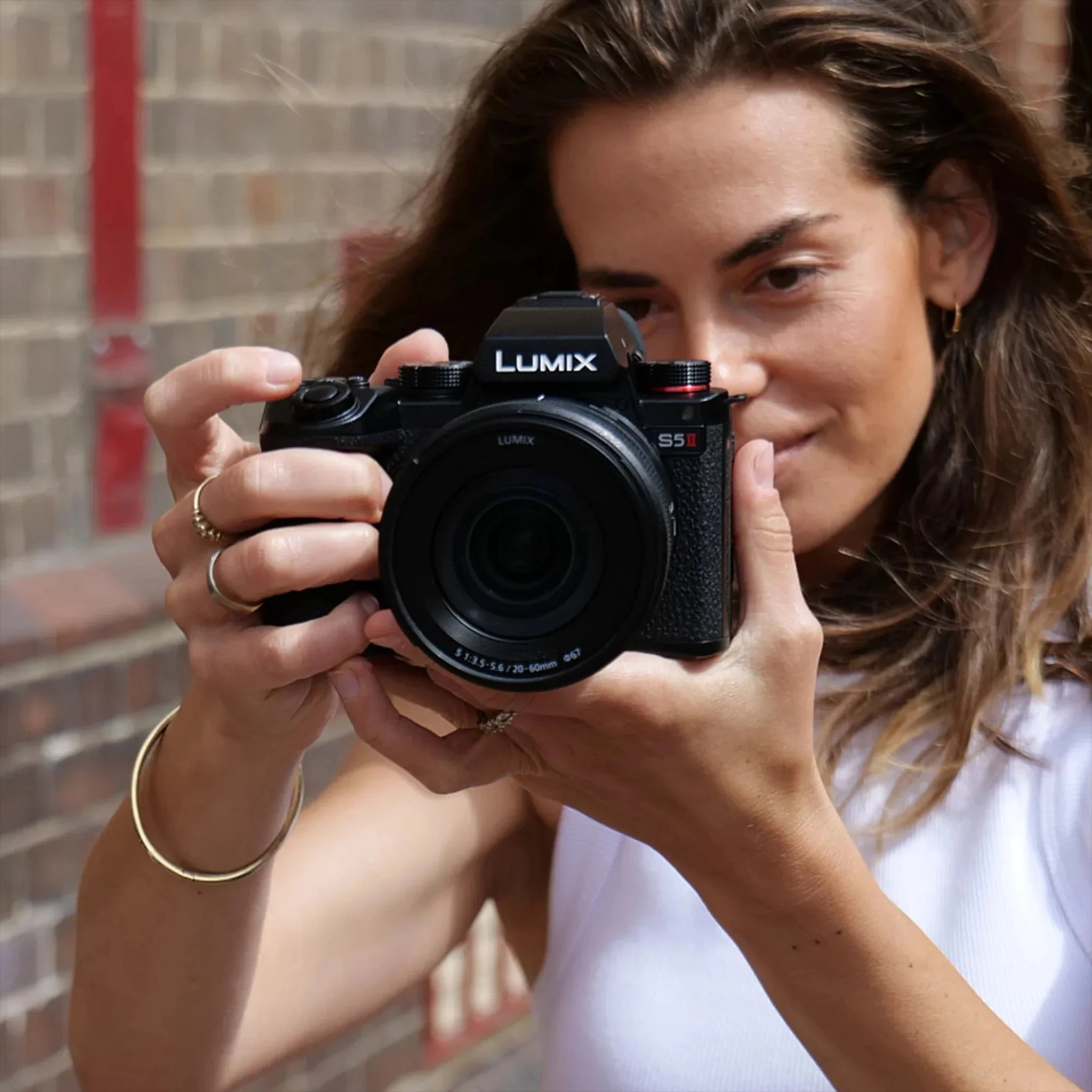 ผู้หญิงยกกล้อง LUMIX S5II ซึ่งเป็นรุ่นที่มี Active I.S. ขึ้นเล็งถ่ายหน้าผนังอิฐ