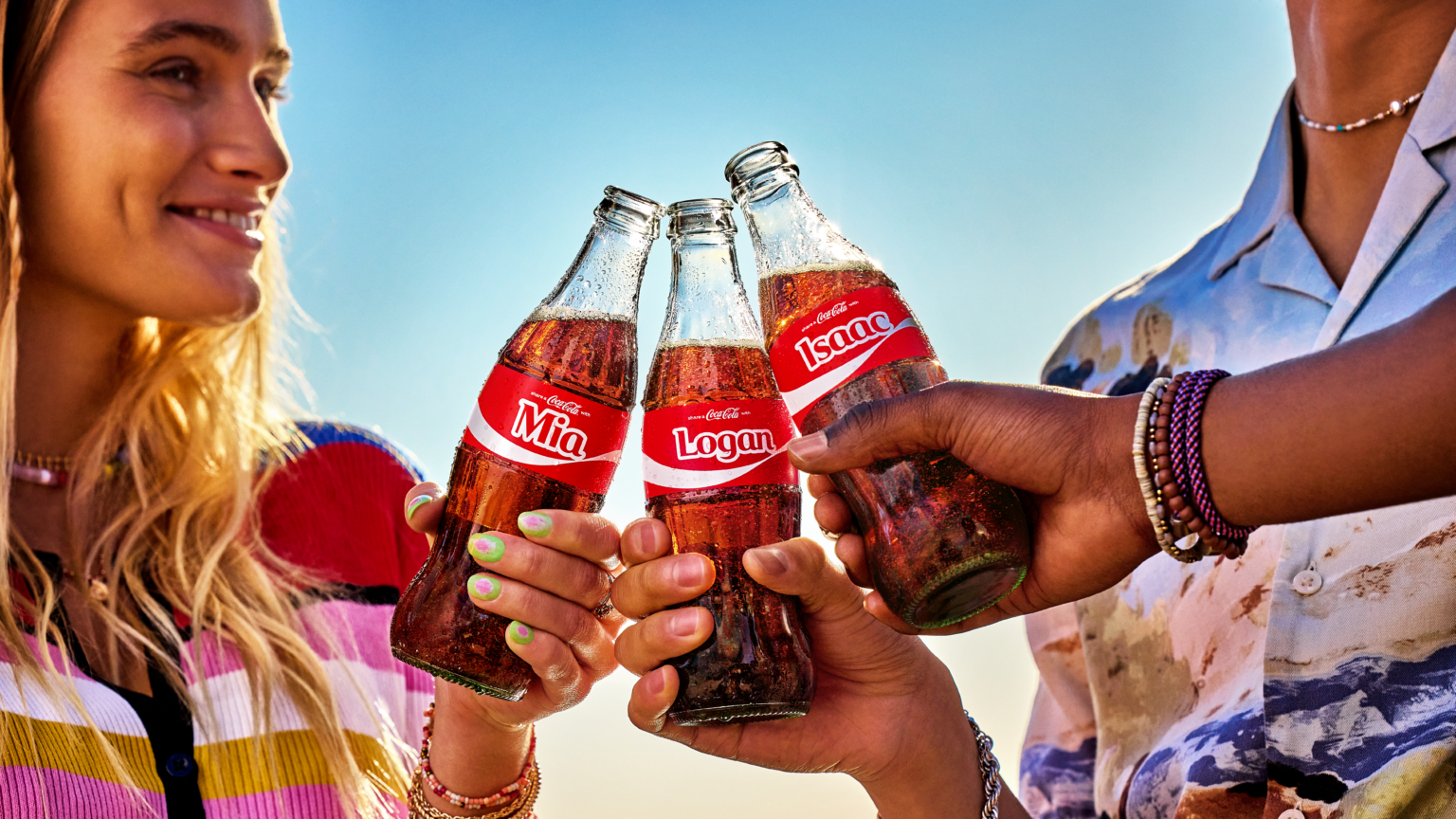 กลุ่มเพื่อนชูขวด Coca-Cola ที่มีชื่อบนฉลาก ภาพแคมเปญ Share a Coke ปี 2025 ที่ชวนคนทำ UGC