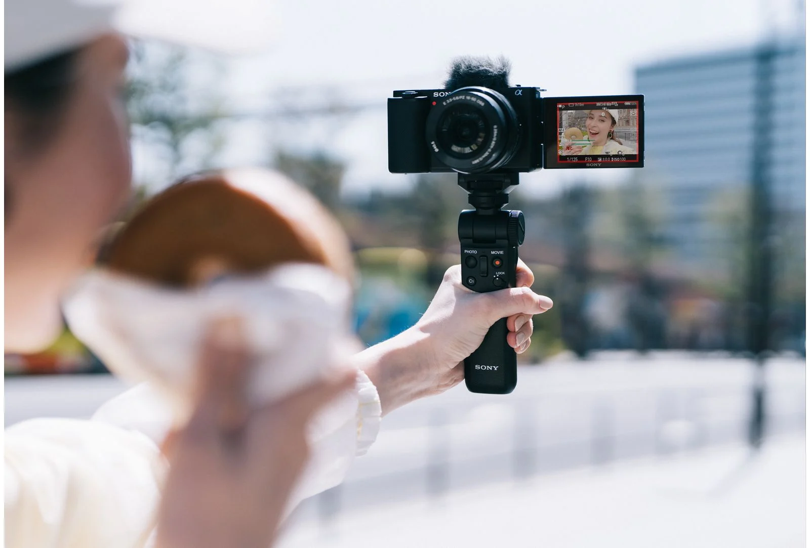 คนถือกล้อง Sony ZV-E10 ติดด้ามจับถ่ายวิดีโอตัวเองกลางแจ้ง